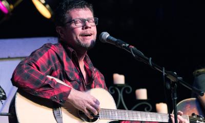 Lee Thomas Miller, in plaid flannel shirt singing on a stage