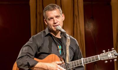 Sam Pacetti with guitar, speaking into microphone