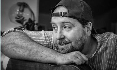 musician Jim Johnston in a ball cap, leaning on his guitar