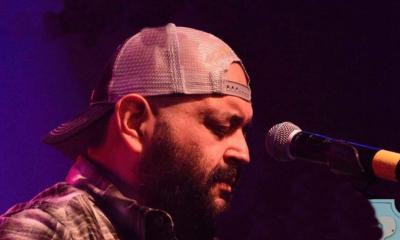 Jon Q., in profile, wearing a basball cap and facing the microphone