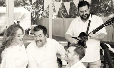 In black and white, the four members of the Pinnacle Singers, wearing white, one with a guitar