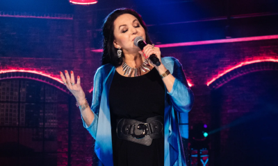 Crystal Gayle lifts her hand and sings on stage with her eyes closed.