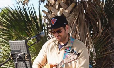 Musician Jeremy Price playing guitr outside, in front of a palm tree