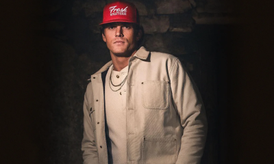 Parker McCollum wears a bright red cap while standing in front of a textured backdrop.