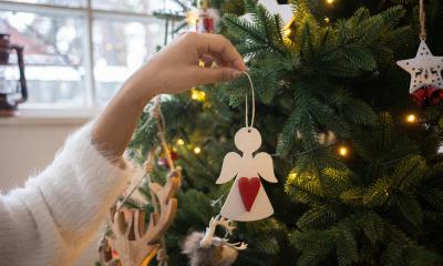 A woman hangs a white angel on a tree decorated in gold and white ornaments