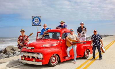 The band Landfall, with instruments, posed around and on an antique red truck near the water on A1A