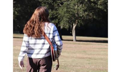 Paige Bechtold walking away from camera, with her banjo.