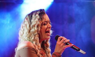 Ashley Estevez on stage with a microphone in front of a blue background