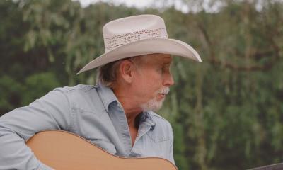 Singer songwriter Wyn Varble with guitar, sitting outside with woods in background
