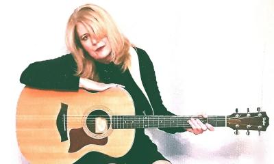 Sparrow Smith (Kathi Witkowski) with her guitar sitting against a white background