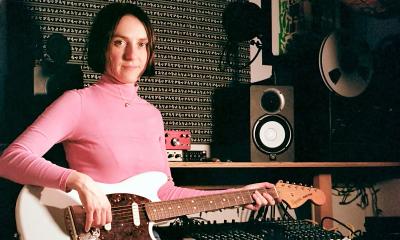 The leader of the band Slippers, wearing a pink turtleneck, in a music studio playing electric guitar