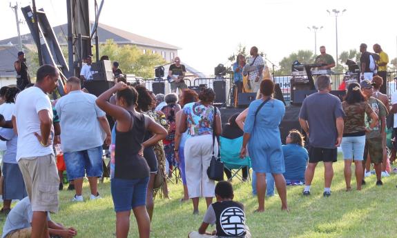 An audience stands on a lawn listening to a Raggae band at a daytime festival.