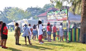 People stand in line at a Jerk food vendor at an outdoor festival.