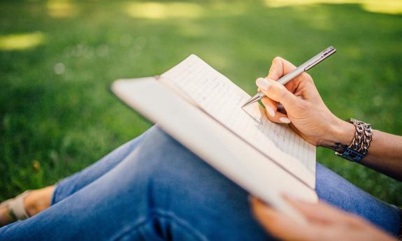 Partial photo of a woman writing on a note pad on her knees