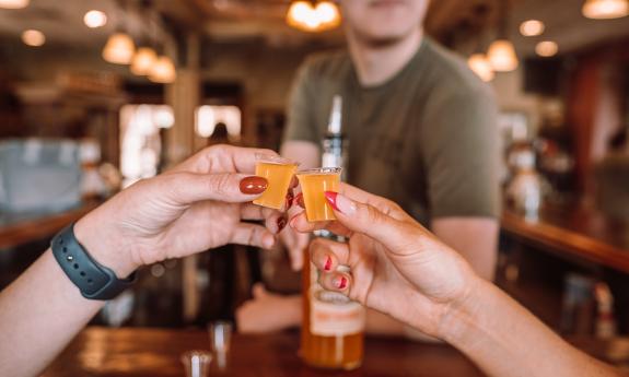 The hands of two women, holding tasting glasses of drinks from City Gate Spirits with the host in the background