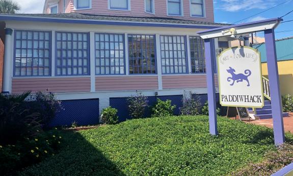 A close up view of the sign and location of Paddiwack, a store in an hold home, painted pink with blue trim and with multi-paned windows