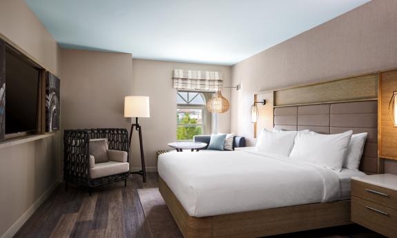 A modern hotel room, with beige walls and wood and brass accents and white bedding