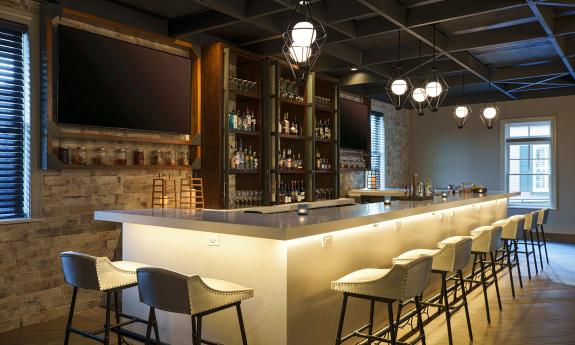 A bar with cream top and chairs, wood paneling and beams, and white and black lights