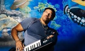 Musician VIBE RW in a graphic design holding keyboard with a fish backdrop. 