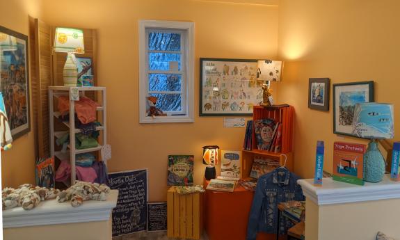 Lamps. fabric art, and small framed art in a yellow-painted alcove of a gallery