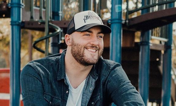 Matt McKinney photo sitting on steps with a baseball hat on. 