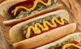 Hotdogs with relish and mustard are slanted on a table. 