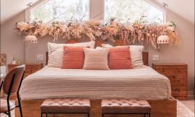 A king-size bed decorated in tones of peach in front of a peaked window