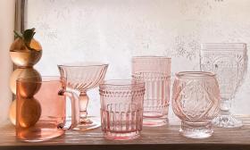 A shelf of colored glassware against a lace curtain