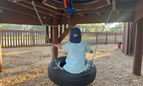 Little boy with Visit St. Augustine baseball cap on while seated on a tire swing at playground in St. Augustine. 