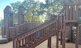 A sideview of the wooden playground with stairs leading to a plank