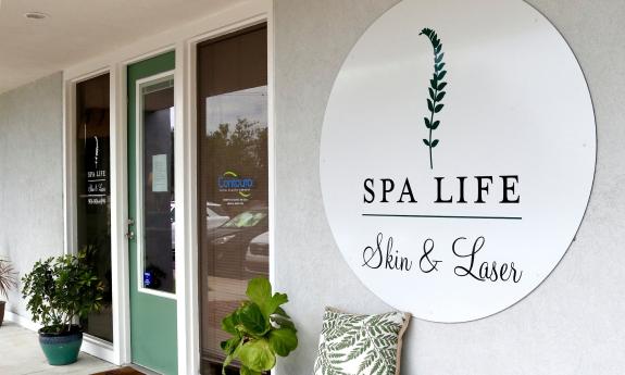 A green entry door with windows on the side, plants, and a green and white sign