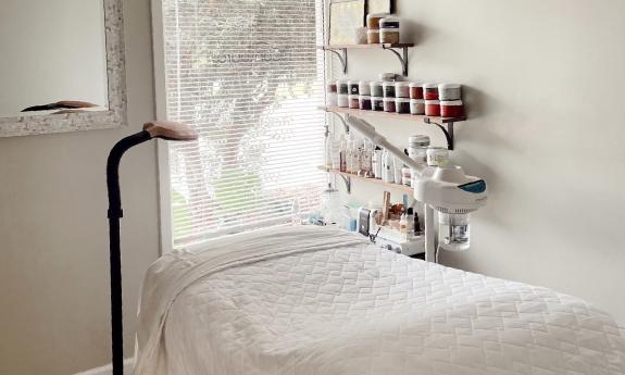 A treatment room at a spa, with a window, mirror, white sheets and colorful products