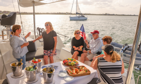 Six people on the deck of a luxury catamaran, enjoying food and beverages