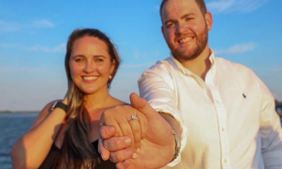 A couple against the sea and sky, showing her new engagement ring