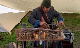 A worker in 16th century garb working at his tool bench, full of hand tools