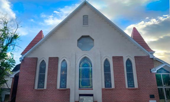 A red bruck church building towering above with several long stained glass windows and two spires