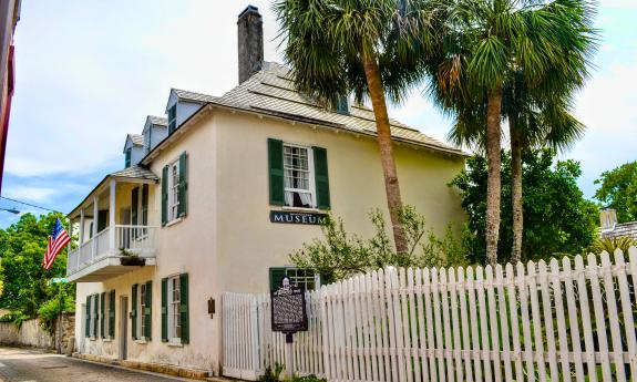 A large coquina house with a white fence extending into the foreground, the house sits on Aviles Street in St. Augustine, Florida