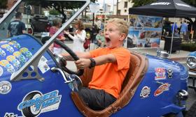 An excited young boy, sitting in a classic roadster at one of the stops for the Great Race