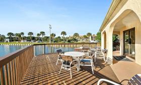 The deck of the clubhouse at Ocean & Racquet Resort has round tables, chairs, and a view of the pond