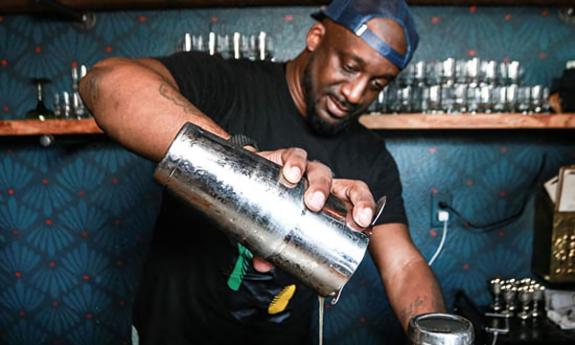 Bartender Josh Davis, mixes one of his signature cocktails in a bar with a teal wall 