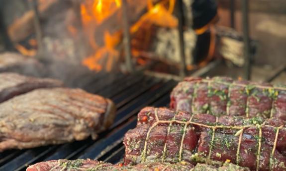 Seasoned meat prepared to be cooked on the live fire grill that is in the background