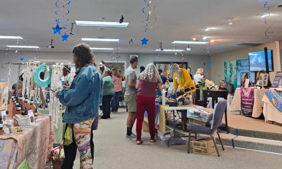 People visit various booths and tables at the Mystic Faire, in a large room decorated with hanging blue stars
