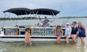 Guests enjoying a cruise on the Tiki Island Adventures deck boat, stand in shallow water next to the boat during a visit to a beach