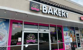 Storefront of Cravings and More Bakery in St Augustine FL. Doors are decorated with hot pink and their cursive gold logo is visible next to the word BAKERY