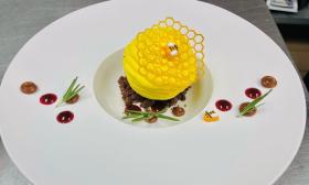 A gourmet dish topped with honeycomb and edible bees is positioned on a plate. 
