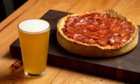 A delicious pan pizza with beer is positioned on a table.