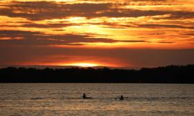 Two people kayak in the water during sunset.
