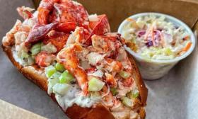 A lobster roll and coleslaw is positioned on top of parchment paper