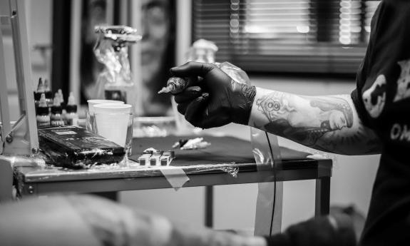 A tattoo artist gathers his equipment and prepares to service a customer. 