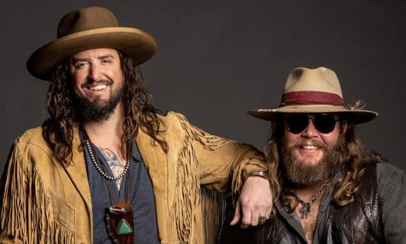 The two musicians in War Hippies, standing relaxed, in buckskin and big hats